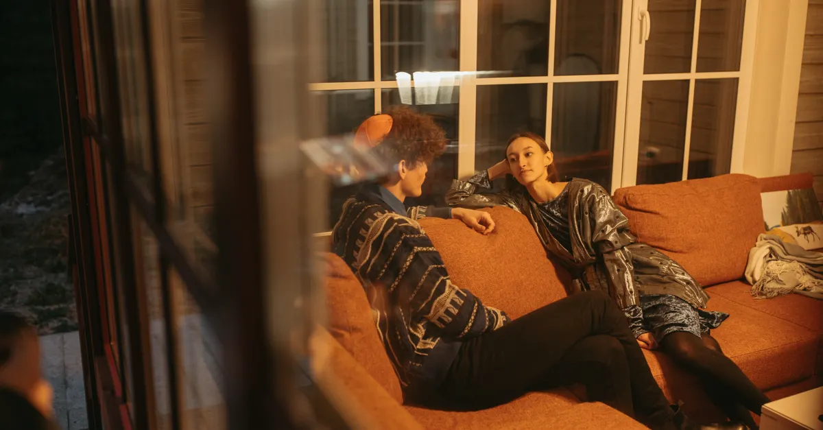 Two adults sitting on a sofa having a relaxed conversation in a warm indoor setting
