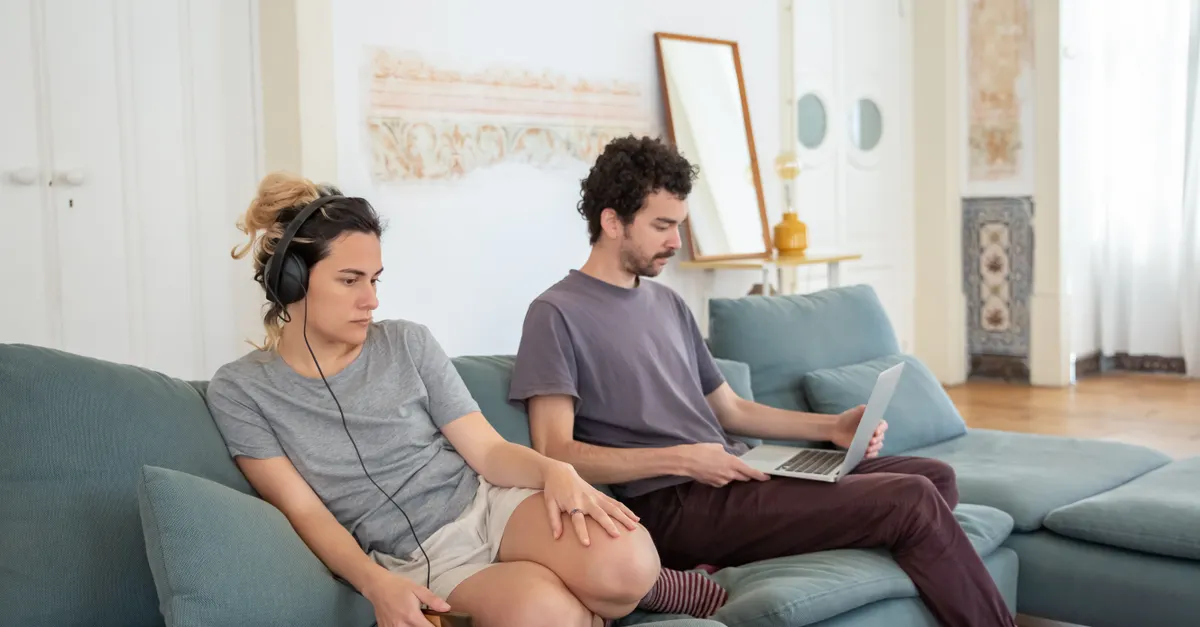 A couple relaxing on a sofa with headphones and laptop, creating a cozy home atmosphere.