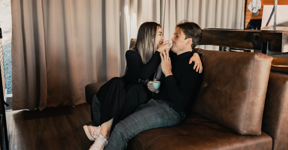 A happy couple laughing together over coffee on a cozy indoor sofa