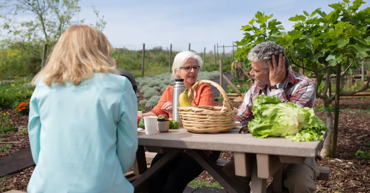 Senior adults at a picnic table enjoying a meal in a vibrant garden setting.