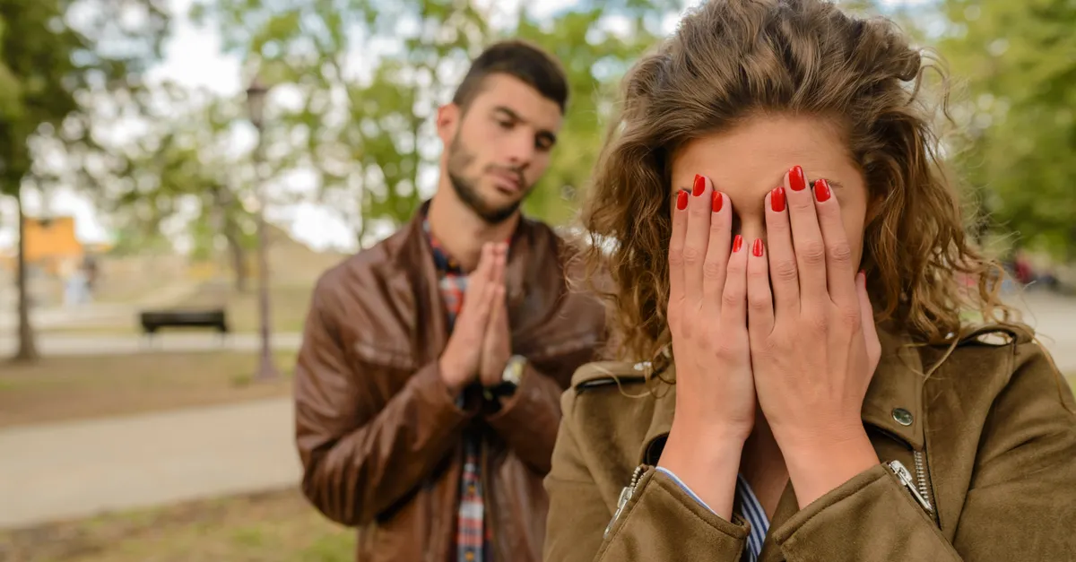 A man apologizes to a woman who covers her face in a park.
