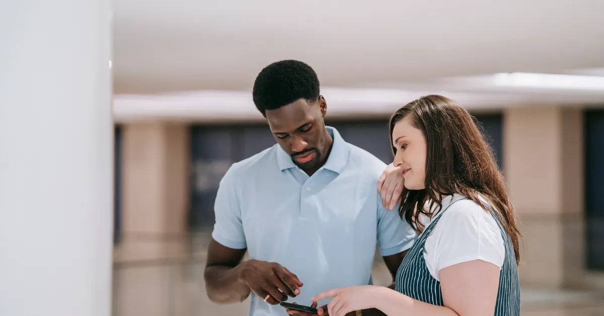 A couple sitting indoors, looking at a smartphone together with focused expressions.