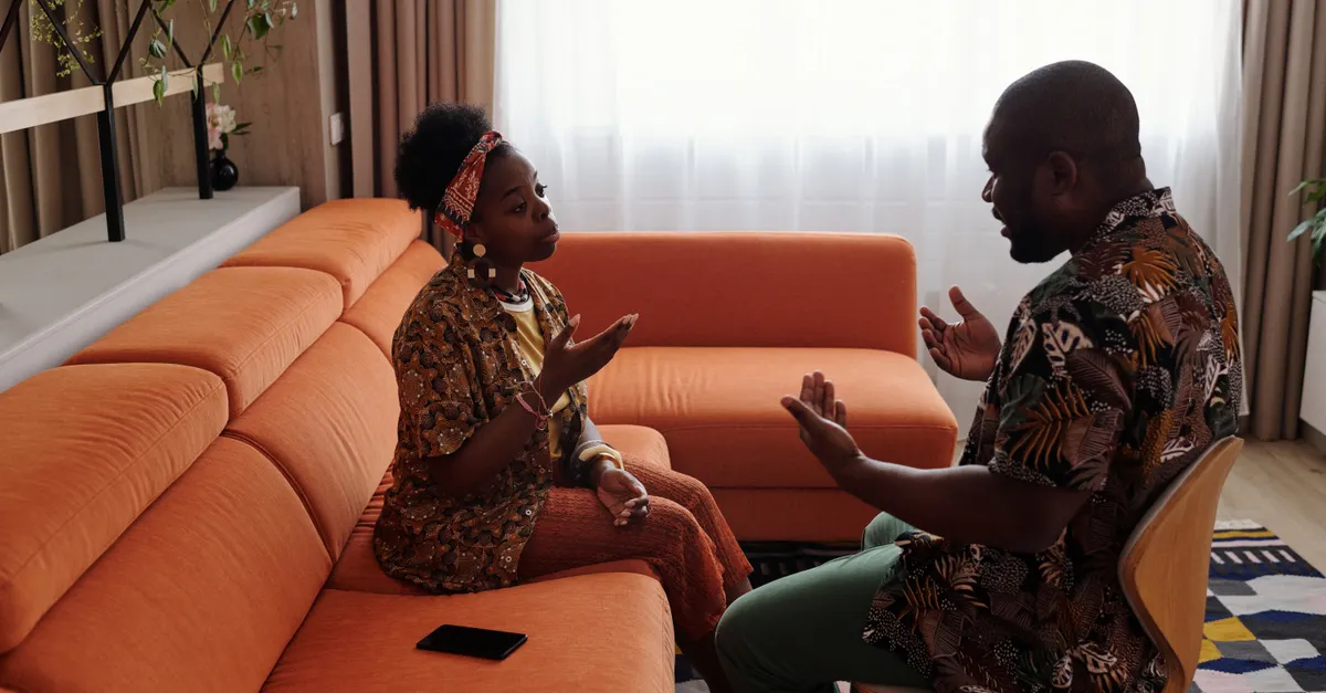 A couple having an emotional discussion on an orange sofa in a modern living room.
