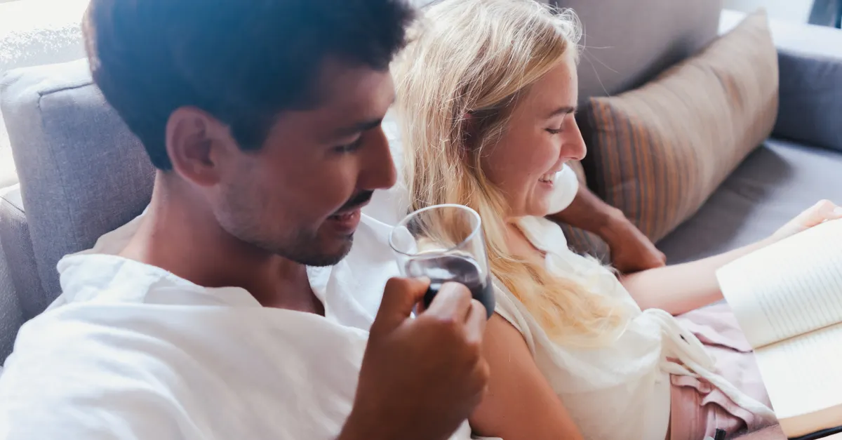 Couple drinking coffee and reading a book together on a sofa.