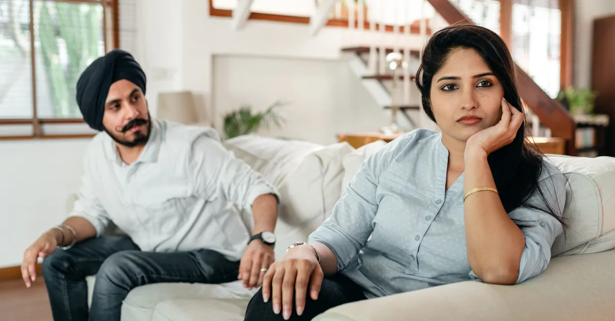 A couple sits pensively on a couch, looking away, after a quarrel.