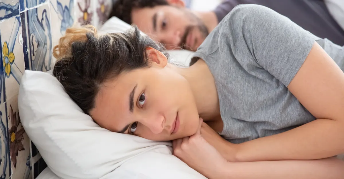 A couple lying in bed with a decorative tiled wall behind them.