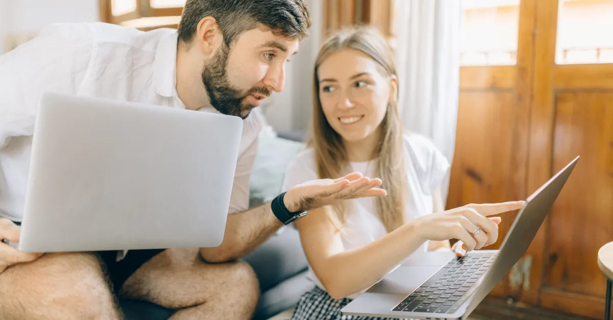 Young couple sitting together, discussing something on their laptops in a cozy room.