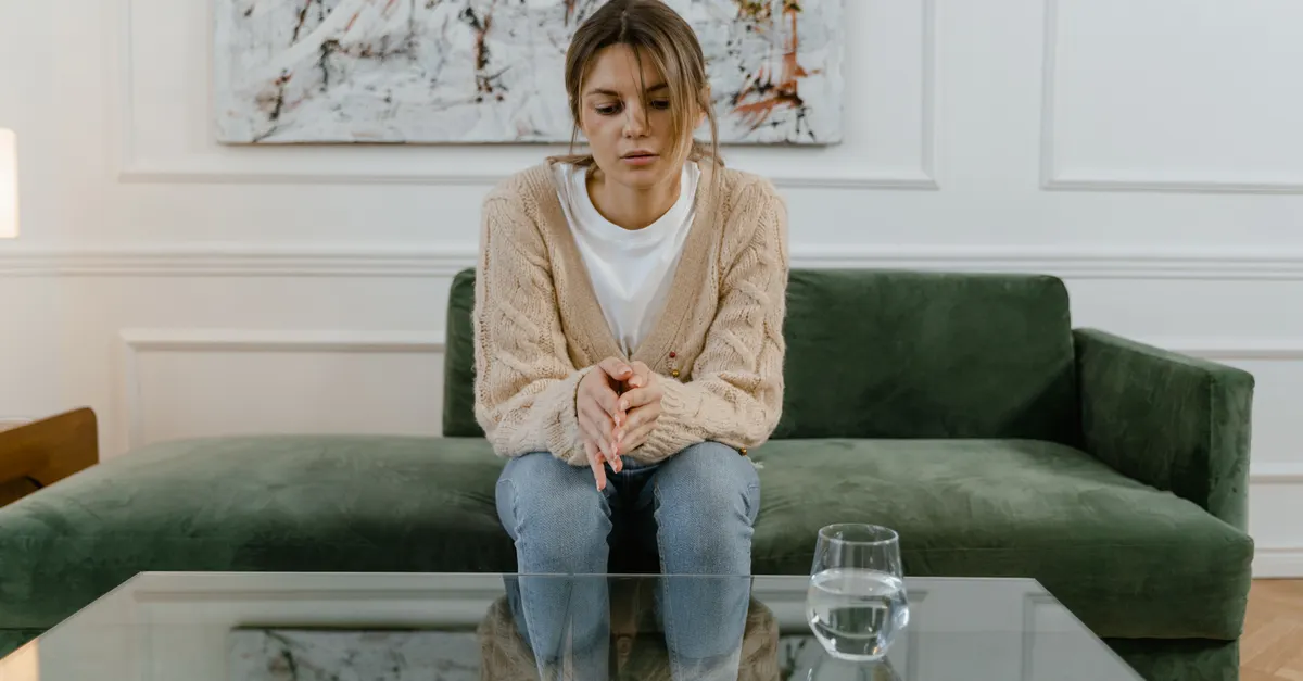 Woman sitting on a green sofa with a pensive expression, reflecting indoors.