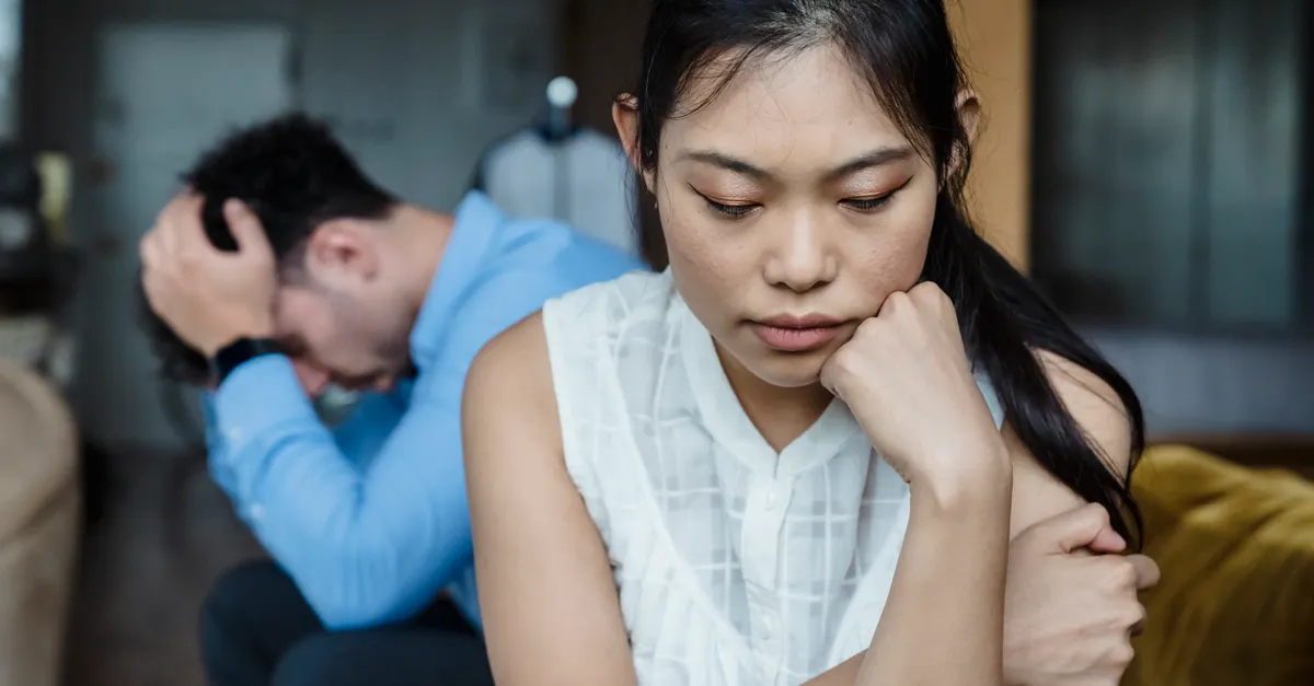 A couple sitting silently on a sofa, appearing tense and distant.