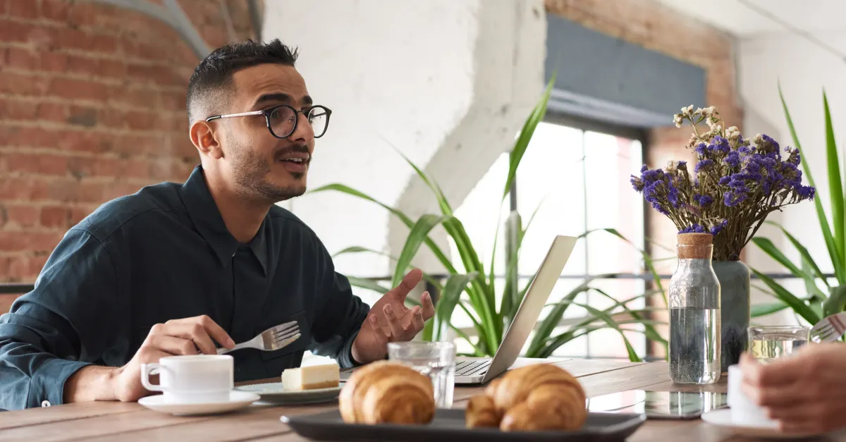 A man in glasses talking over brunch with croissants and coffee at a table