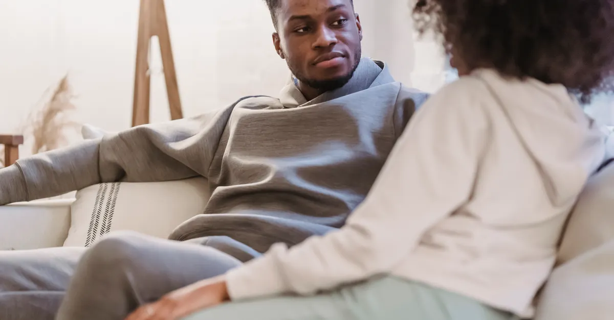 A man listens to a woman relaxing on a sofa in a lounge.