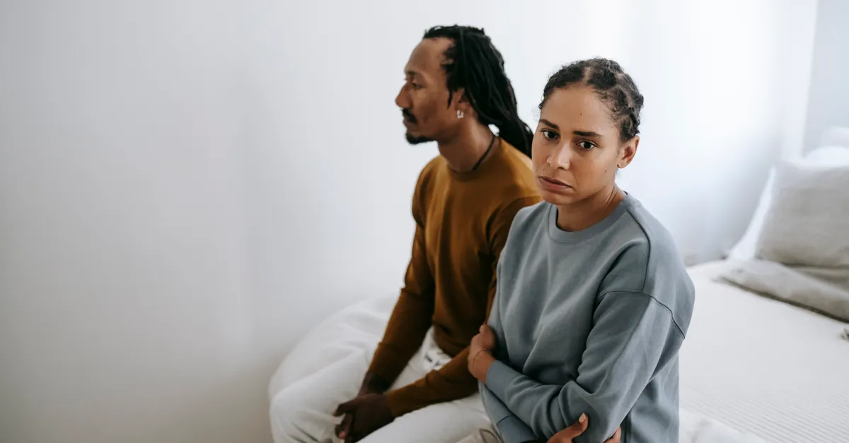 Frustrated thoughtful African American couple in casual wear sitting close on soft bed after quarrel