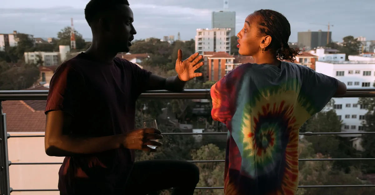 A couple in vibrant attire engages in conversation on a city balcony at sunset.