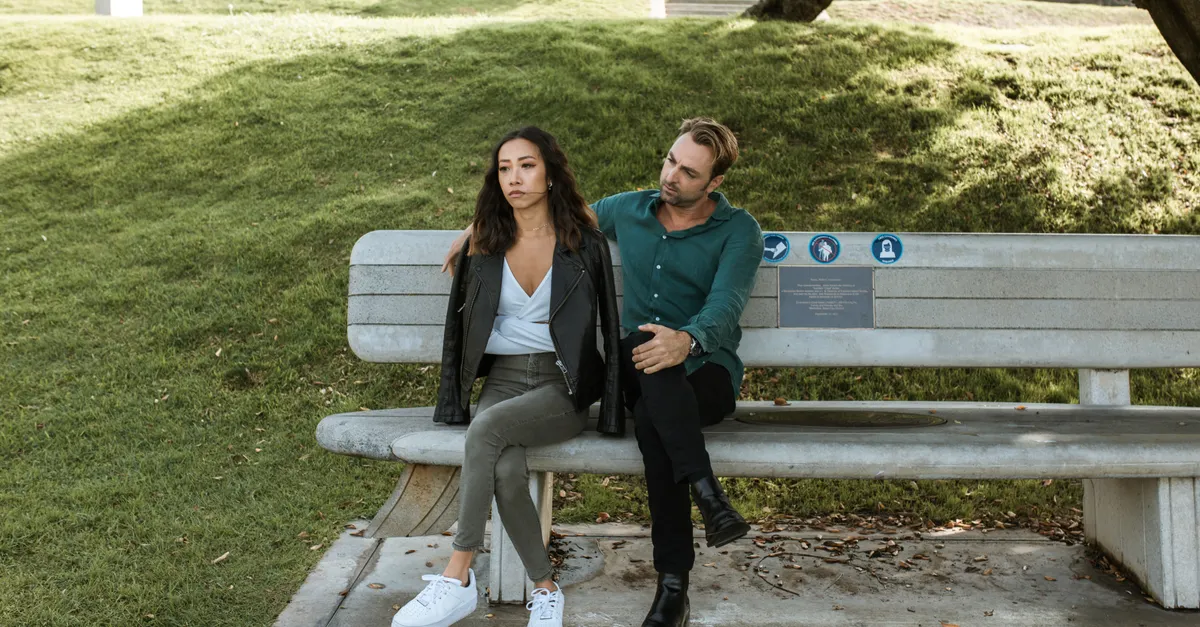 A couple having a serious discussion on a park bench during the day.