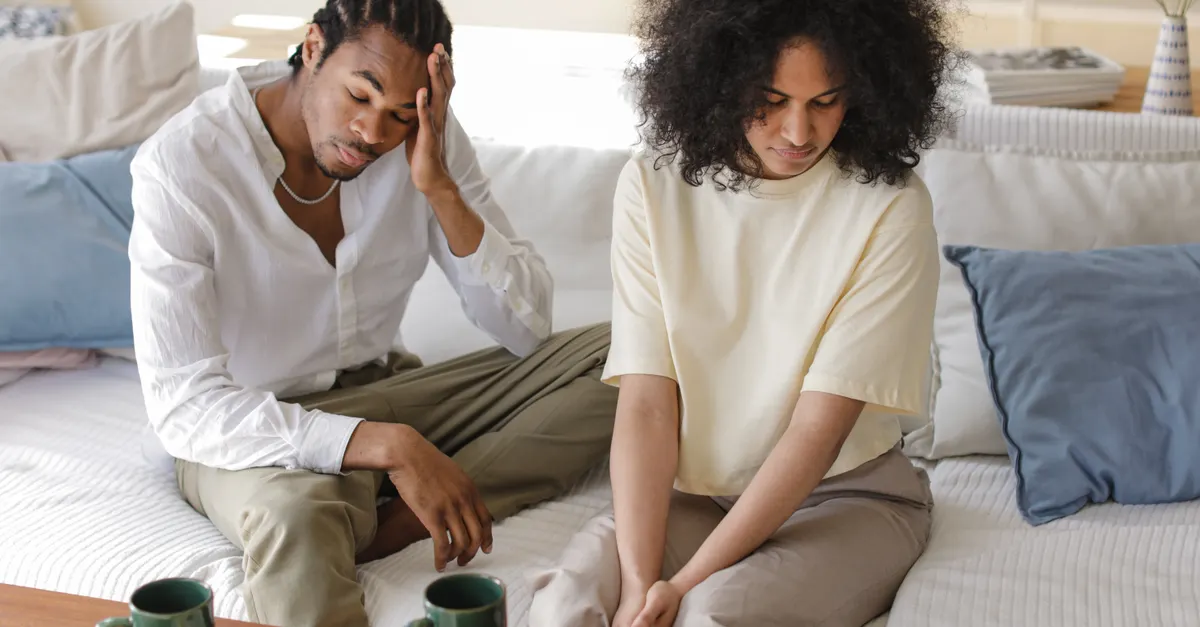 Black couple sitting contemplatively on a modern sofa indoors.