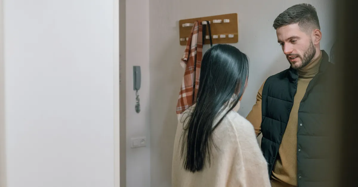 A man and woman talk inside a cozy home, appearing engaged in conversation.
